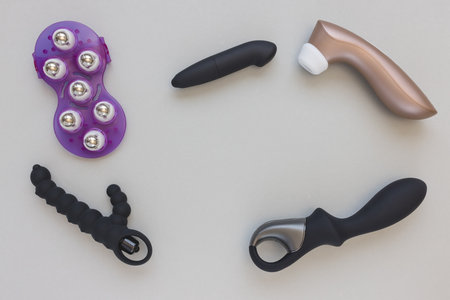 Variety of pink and black sex toys for adult man and woman on gray background. Dildo vibrator, clitoral stimulator, butt plug, rabbit shaped vibrator to satisfy all preferences and areas of body. Top view, copy space in the centerの写真素材