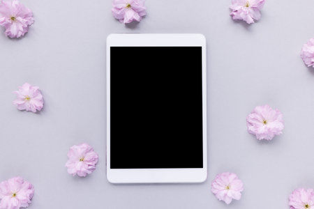 Digital tablet and spring sakura cherry blossom flowers, pastel pink background. Online shopping,...