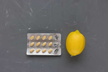 Empty blister packs of pills and lemon on dark gray background, supplement of vitamin C concept....