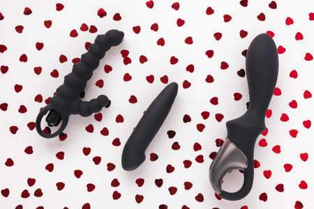 Three black sex toys for adult man and woman on white with red foil hearts Valentines Day...