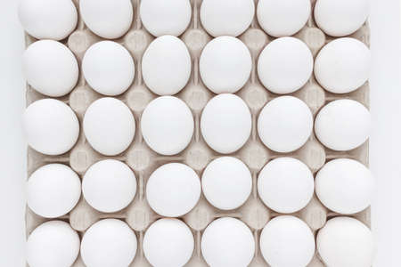 Fresh raw 30 pack of large white eggs in cardboard on white background. Consumerism, egg production,...