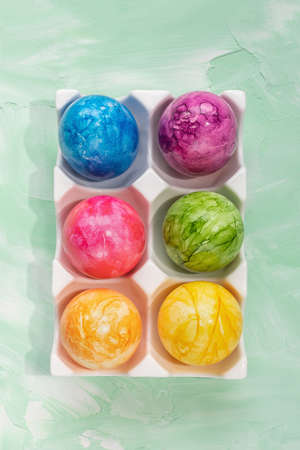 Colorful eggs in porcelain storage organizer box on green background. Easter celebration concept....