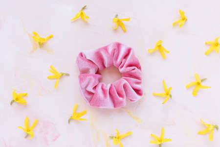One trendy velvet scrunchie and fresh spring yellow flowers on pastel background. Flat lay, top...