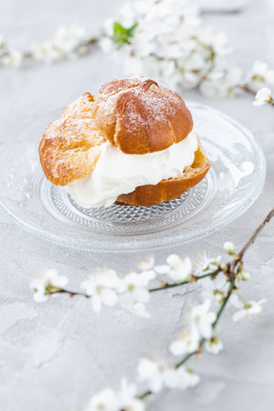 Choux Bun with whipped cream and sugar powder on top on glass plate. Gray background with spring...