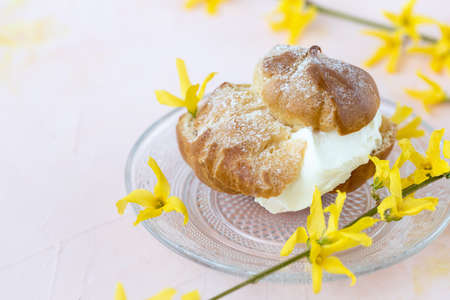 Choux Bun with whipped cream and sugar powder on top on glass plate. Pink background with spring...