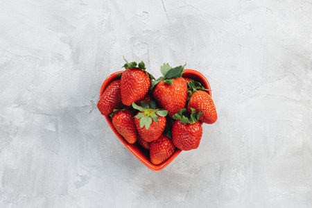 Fresh-picked strawberries in heart-shaped bowl on rustic gray background, concept of healthy eating vegan food. Summer snack. Closeup, selective focus, copy spaceの写真素材