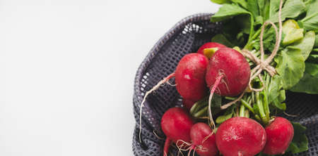 Bunch of fresh dirty organic ripe red radish with green leaves in eco-friendly reusable produce bag...