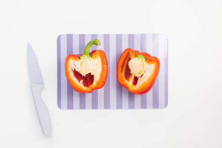 Fresh organic ripe sweet red bell pepper cut in half on cutting board with knife on white...
