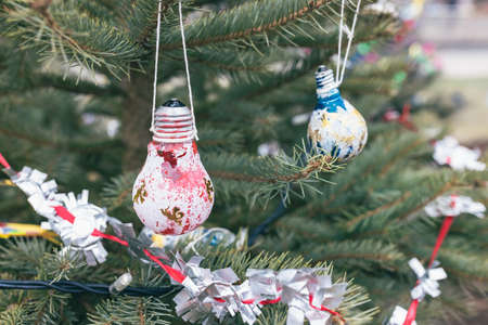 Painted white, red, blue and gold old light bulb decoration on Christmas tree. Diy creative ideas. Environment, recycle, reuse, upcycling, zero waste, electricity concept. Selective focusの写真素材