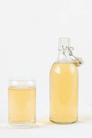 Homemade kombucha fermented drink in glass and bottle on white background. Heathy probiotic beverage with bubbles. Summer non alcoholic drinks. Copy spaceの写真素材