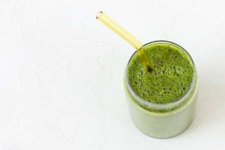 Green smoothie in glass with environmentally friendly drinking glass tube. White background. Vegan, raw, clean, healthy foodの写真素材
