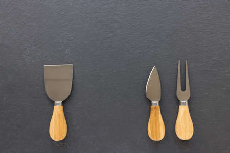 Set of cheese knives with wooden handles. Fork and spatula on black background. Shabby appearance. Top view, copy spaceの写真素材