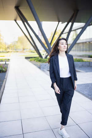 Full body portrait of Asian confident business woman in suit, walking in business center spring, summer or fall park. Job career, office work, business people lifestyle conceptの写真素材