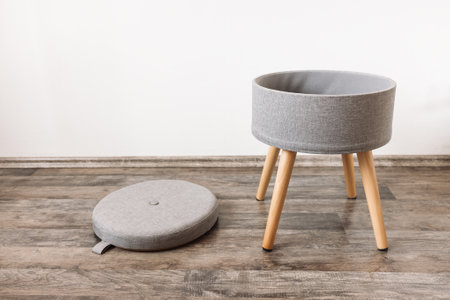 Trendy stool with and build-in storage space. Side view, white wall, copy space. Modern mulrifunctiional chair with wooden legs and removable lid. Round gray linen poufの写真素材