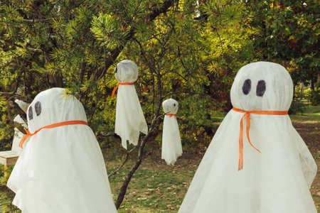 Halloween ghosts decoration hanging on tree branches. Easy autumn DIY outdoor yard decor and holiday...