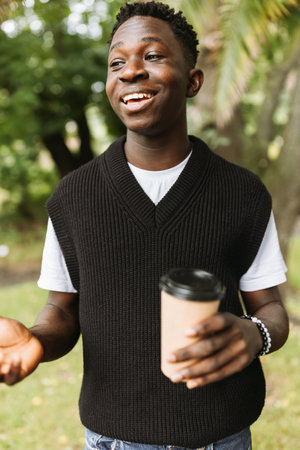 Young African American man smiling with to go coffee cup on street outdoor. Young black student on...