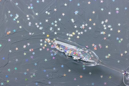 Champagne flute glass on black with colorful stars confetti festive background. Winter holiday, New Year party and celebration concept. Creative flat layout with copy spaceの写真素材