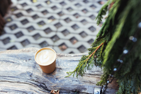 Takeaway coffee in paper cup on old rustic wooden bench in coffee shop with outdoor space with eco-friendly garden. Fall or winter garden with pine branchの写真素材