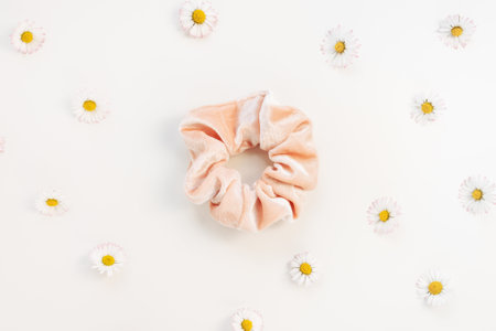 One trendy pink velvet scrunchie and fresh spring daisy flowers on whitel background. Flat lay, top...
