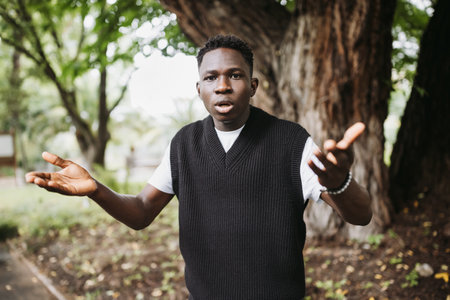Shocked surprised young African man with hands up in park or street. Frustrated young male shrugging...