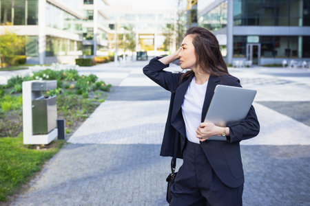 Relaxed and confident Asian business woman in suit holding laptop, outdoor. Job, work aspirational concept, background of office center. Business people lifestyle, copy spaceの写真素材