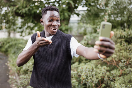 Young happy African man taking selfie or vlogging on his mobile phone. Black student having...
