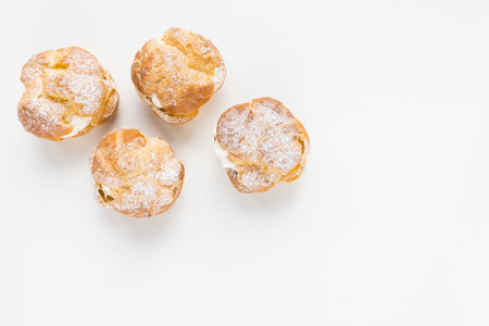 Choux Bun with whipped cream and sugar powder on top on white background. Delicate choux pastry dessert. French cream puff. Top view, copy spaceの写真素材