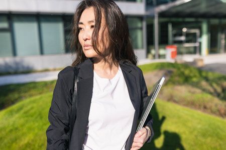 Tired overworked Asian business woman in suit holding laptop. Stress at work, migraine, frustration and depression concept, background of office center. Business people lifestyle, copy spaceの写真素材