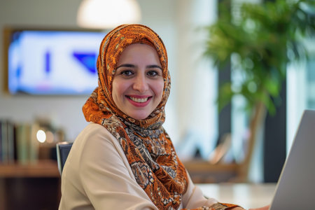 Middle aged Middle Eastern woman in hijab in front of a laptop at modern workplaceの素材