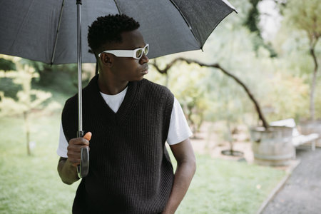 Stylish Black Man with Umbrella Enjoying a Rainy Day Outdoorsの写真素材