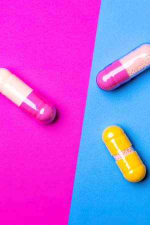 Colorful capsules on pink and blue background, pharmaceutical art.の素材