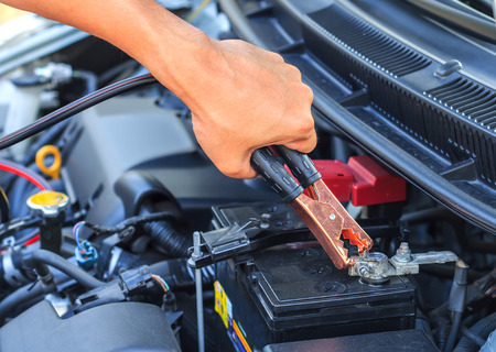 A car mechanic uses battery jumper cables to charge a dead battery