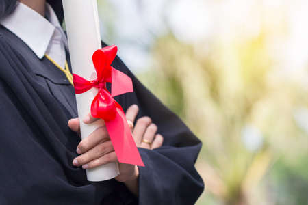 Happy graduate young Asian woman in cap and gown holding a certificated in handの写真素材