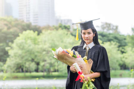 Happy graduate young Asian woman in cap and gown holding a certificated in hand, Education concept