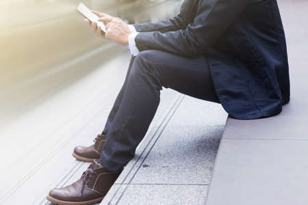 The businessman sitting on stairs and using smartphoneの写真素材