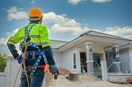 Construction worker wearing safety gear and holding electric drill standing at construction site at...