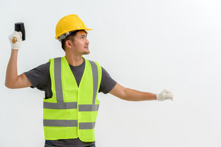 Asian male construction worker wearing hard hat holding rubber mallet making hammer strike gesture...