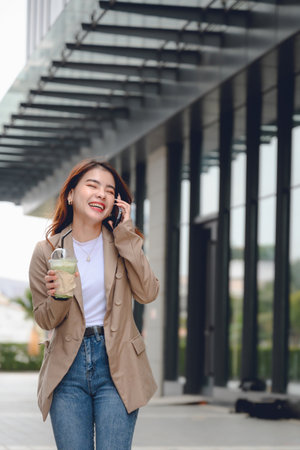 portrait portrait of beautiful asian woman happily walking and talking on the phone close to her office building Smiling woman holding smartphone walking on outdoor streetの写真素材