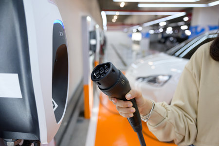 Close-up shot of female hand holding electric vehicle charger connector to charge the car Car park...