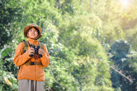Asian woman backpacker nature explorer wearing hat and backpack Young female tourist with binoculars during trekking exploring while walking in nature forest with happy holidayの写真素材