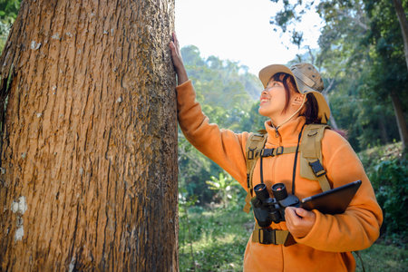 Asian woman nature explorer wearing hat and backpack Attractive young female tourist looks while walking in the natural forest with happiness on vacation.の写真素材