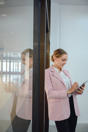 Portrait of a beautiful young business woman Standing confident and smiling company employee holding digital tablet beside glass in officeの写真素材