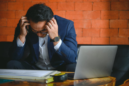 male business man sitting disappointed sad at work wooden desk in the office Sit stressed out planning your construction projects and construction business.の写真素材