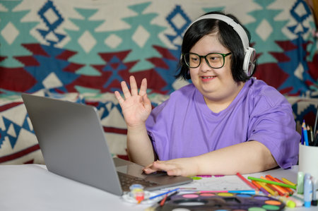 Asian girl with down syndrome in glasses and casual wear using laptop at home. Asian girl with down...