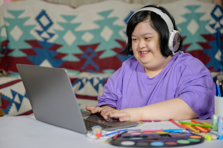 Asian woman with down syndrome wearing casual clothes using laptop at home Asian girl with down syndrome she is happy to learn from internet using laptop at homeの写真素材