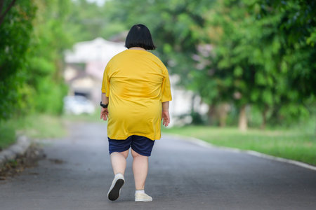 back view fat asian girl exercising By walking to burn fat and jogging slowly, fat woman walks for exercise in a natural park.の写真素材