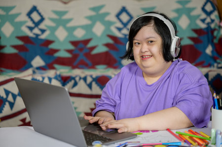 Asian woman with down syndrome wearing casual clothes using laptop at home Asian girl with down syndrome she is happy to learn from internet using laptop at homeの写真素材