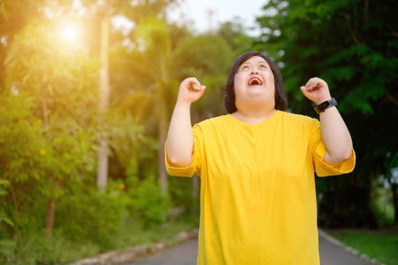 Asian woman with down syndrome doing winner pose with her arms raised Smiling and screaming for success in a natural parkの写真素材