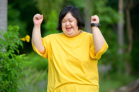 Asian woman with down syndrome doing winner pose with her arms raised Smiling and screaming for success in a natural parkの写真素材