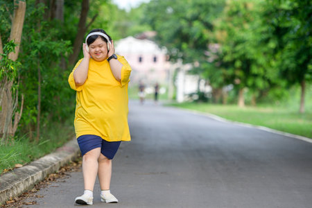 Asian girl with Down syndrome wearing headphones Smile and be happy by walking to burn fat and running slowly to exercise in a park in the middle of nature.の写真素材